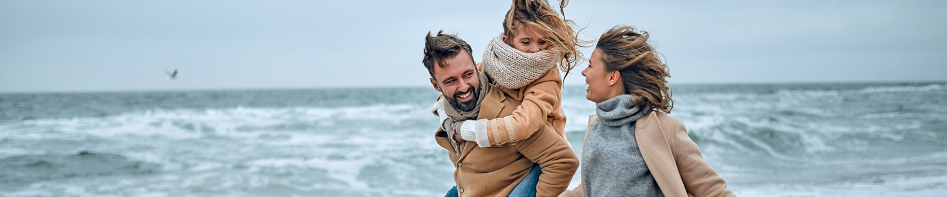 Family on beach with child on fathers shoulders during the winter